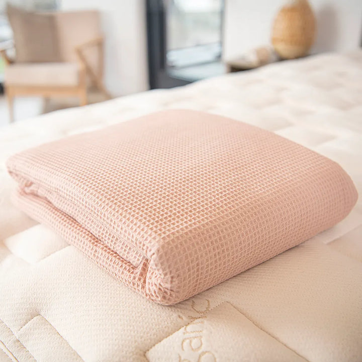Bedroom view Naturepedic Organic Cotton Waffle Blanketsin in Pink folded on mattress