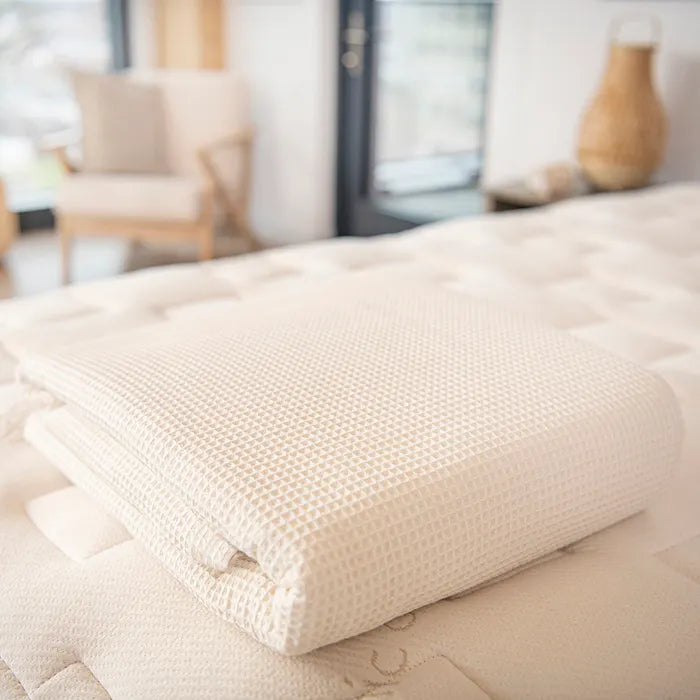 Bedroom view Naturepedic Organic Cotton Waffle Blankets in cream folded on mattress