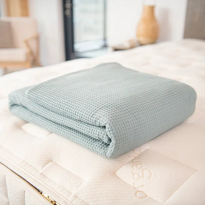 Bedroom view Naturepedic Organic Cotton Waffle Blankets in blue folded on mattress