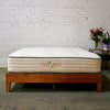 Harvest Green Original Vegan Mattress on a wooden platform bed with flowers on an end table.