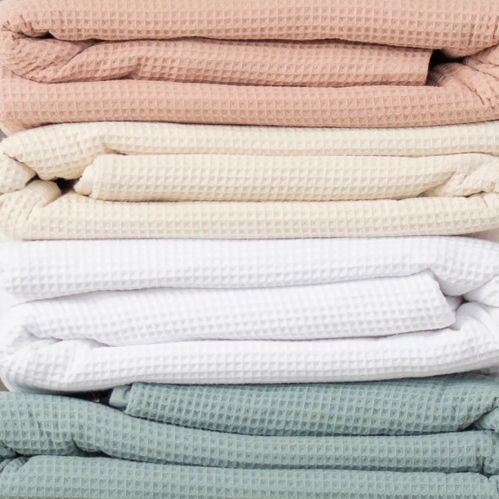 4 different colors of Naturepedic Organic Cotton Waffle Blankets stacked on top of eachother