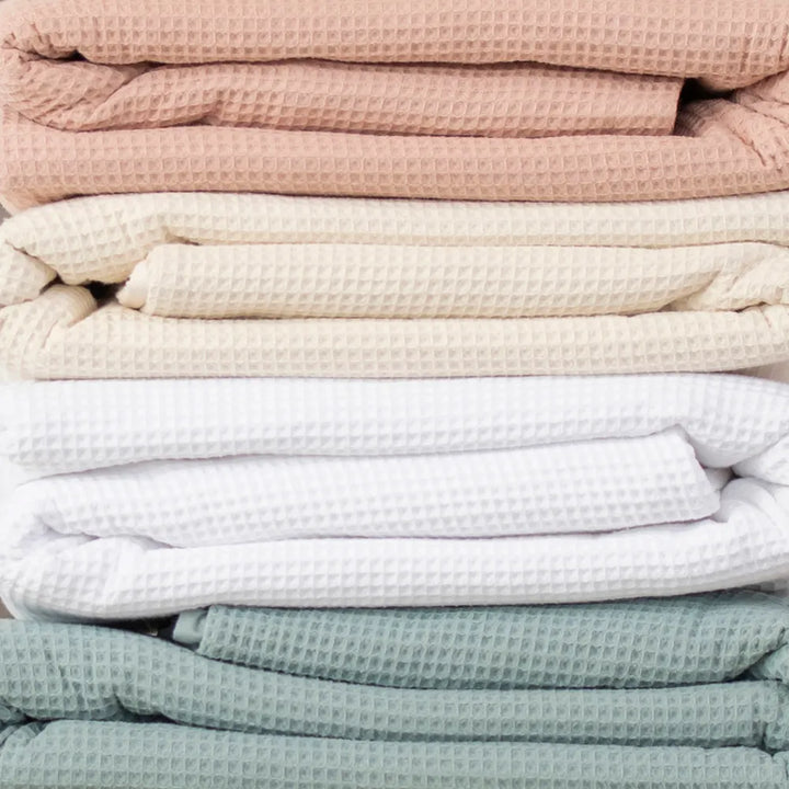 4 different colors of Naturepedic Organic Cotton Waffle Blankets stacked on top of eachother