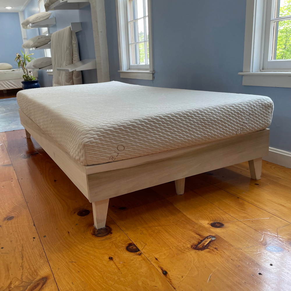 Mattress on a wooden bed frame in a room with blue walls and windows.