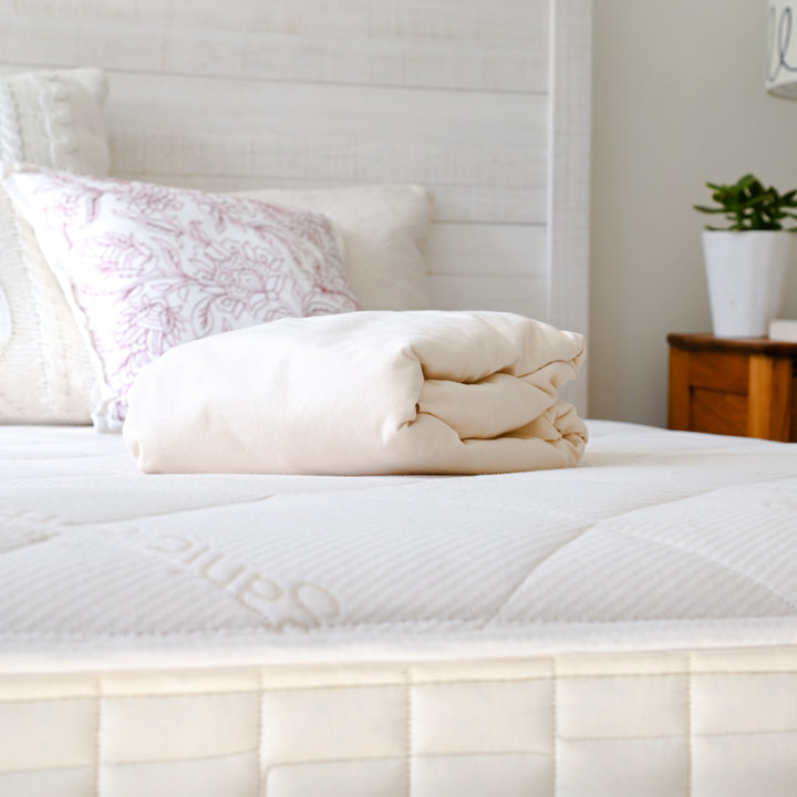 Folded Naturepedic Organic Waterproof Mattress Protector placed on dressed bed 